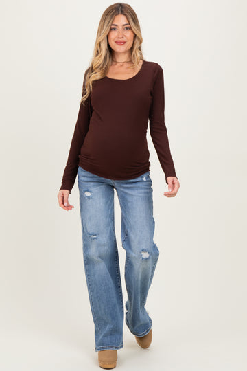 woman wearing a brown long sleeve maternity top and distressed light blue jeans, showcasing her baby bump