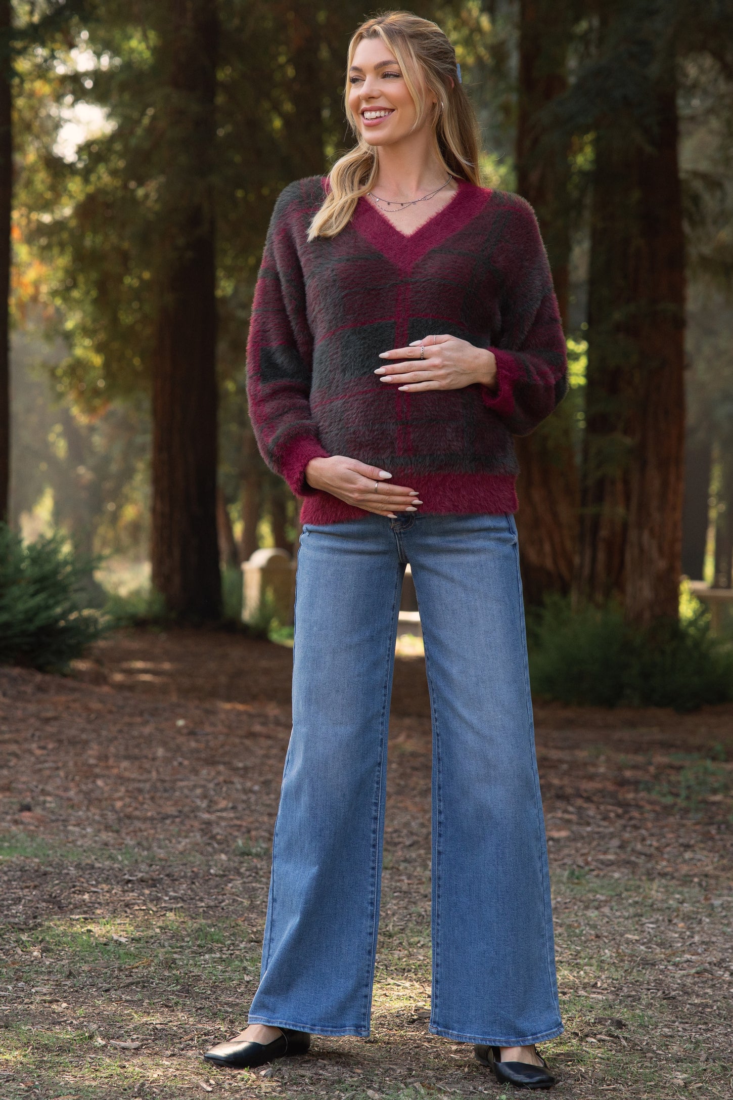 woman wearing a burgundy and gray striped maternity sweater and blue wide-leg jeans, holding her baby bump