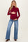 woman wearing a burgundy turtleneck maternity top and blue wide-leg jeans, holding her baby bump