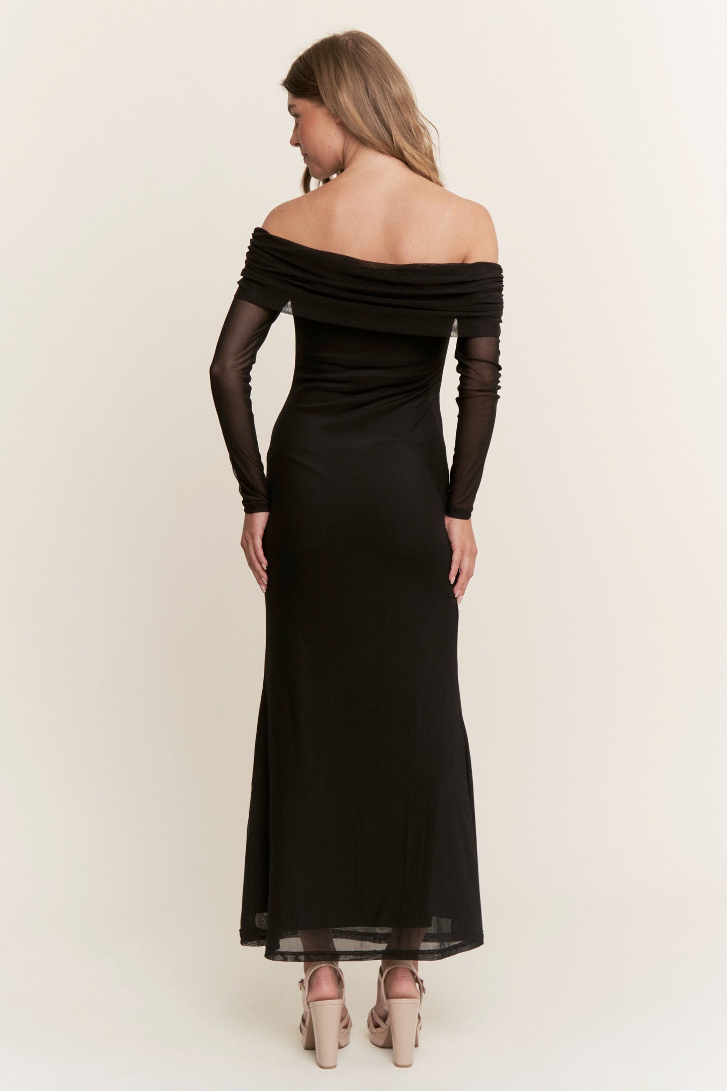 woman wearing a black off-shoulder evening gown with long sheer sleeves and a fitted silhouette