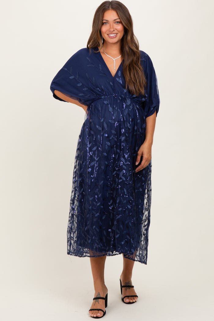 woman wearing a navy blue maternity dress with floral embroidery and a wrap style, showcasing her baby bump