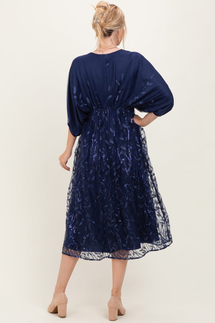 woman wearing a navy blue dress with sheer overlay and flutter sleeves, styled with a fitted waist and mid-calf length