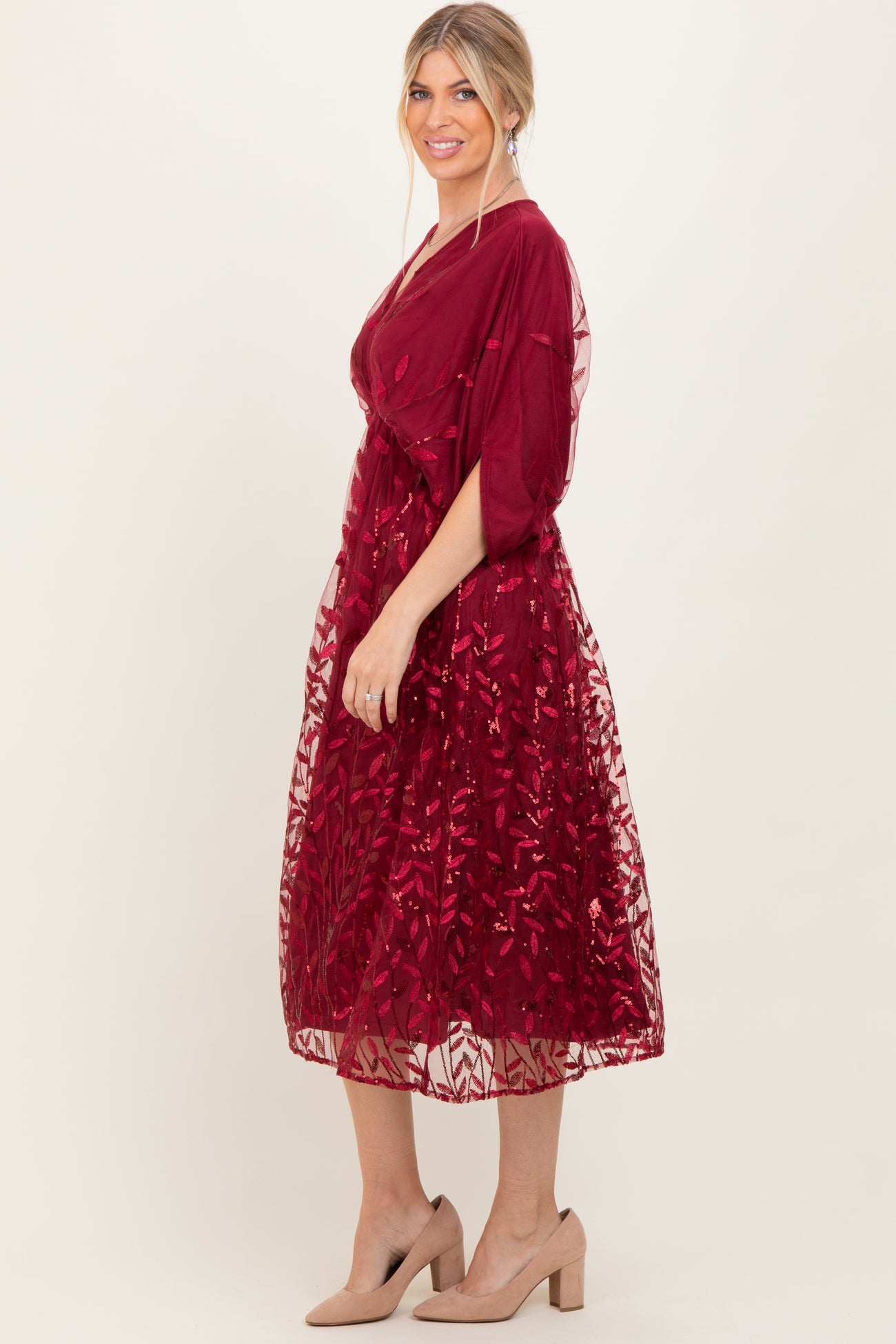 woman wearing a burgundy knee-length dress with floral sequin detailing and short sleeves, paired with nude heels