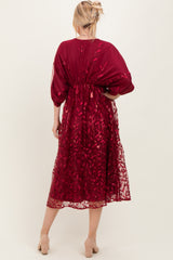 woman wearing a burgundy embroidered maxi dress with sheer overlay and balloon sleeves, seen from the back