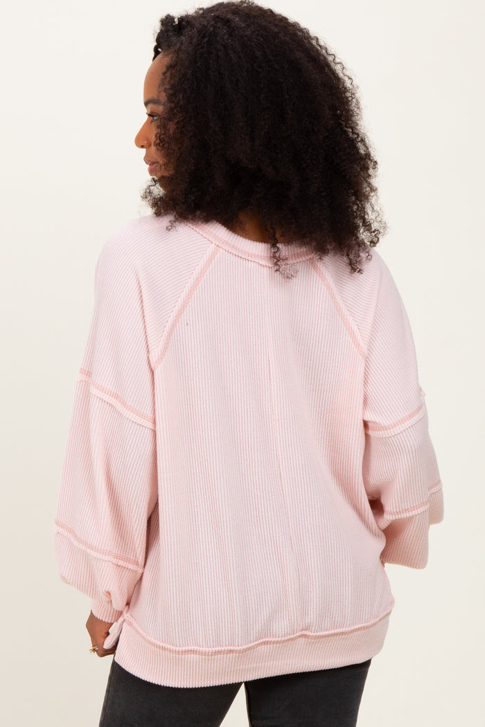 woman wearing a light pink oversized ribbed sweater with three-quarter sleeves and a relaxed fit.