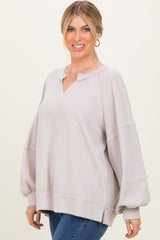 woman wearing a light beige oversized ribbed sweater with a v-neck and balloon sleeves, smiling at the camera