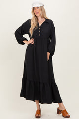 woman wearing a black long sleeve maxi dress with button details and a tiered ruffle hem, paired with a white hat and brown clogs