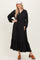 woman wearing a black long sleeve maxi dress with button details and a tiered ruffle hem, paired with a white hat and brown clogs