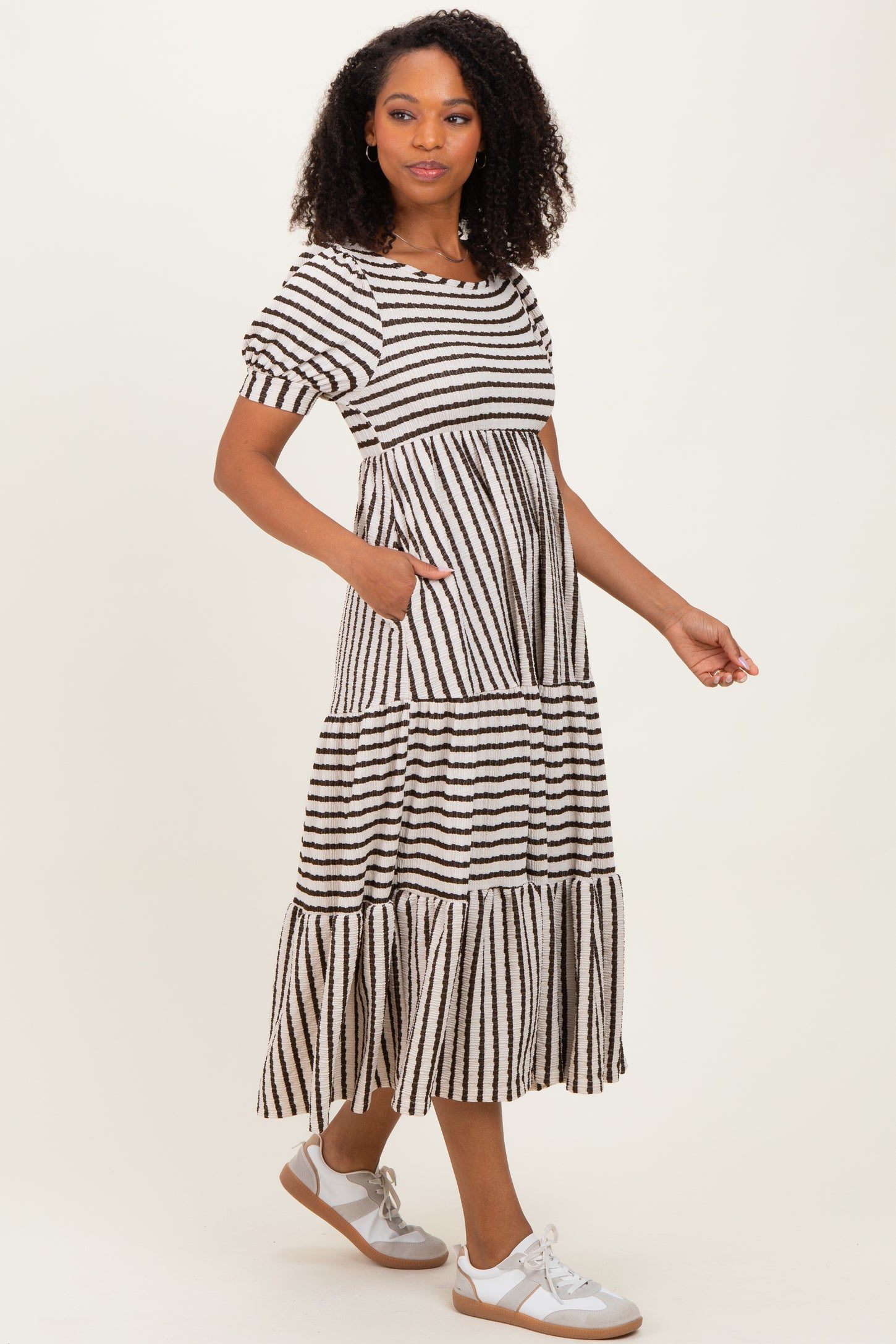 woman wearing a striped black and white maxi dress with short puff sleeves and pockets, paired with silver sneakers