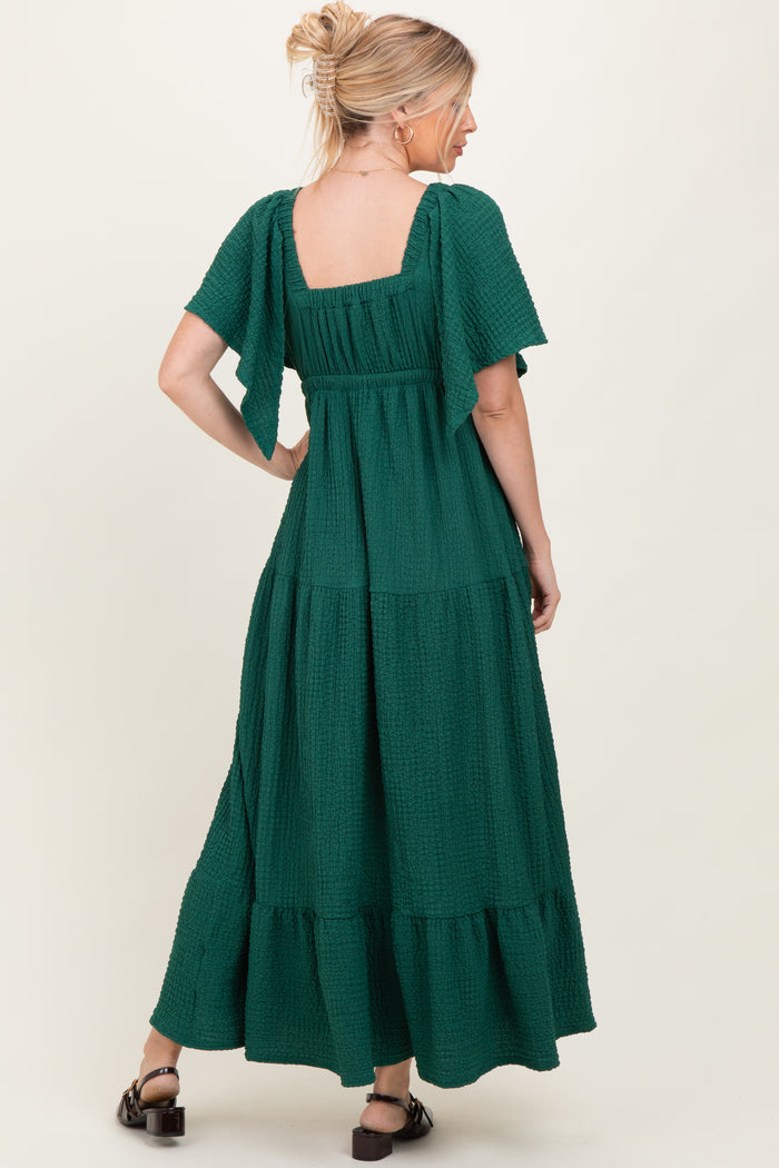 woman wearing a green maxi dress with short flutter sleeves and a tiered design, seen from the back