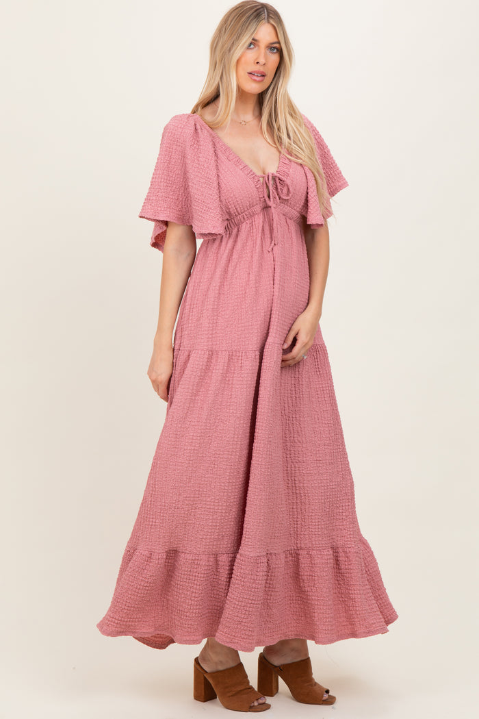 woman wearing a pink wrap maxi dress with flutter sleeves and a tiered hem, standing in a casual pose