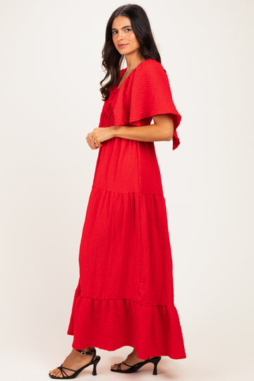 woman wearing a red tiered maxi dress with ruffle sleeves and a bow detail, standing sideways against a plain background