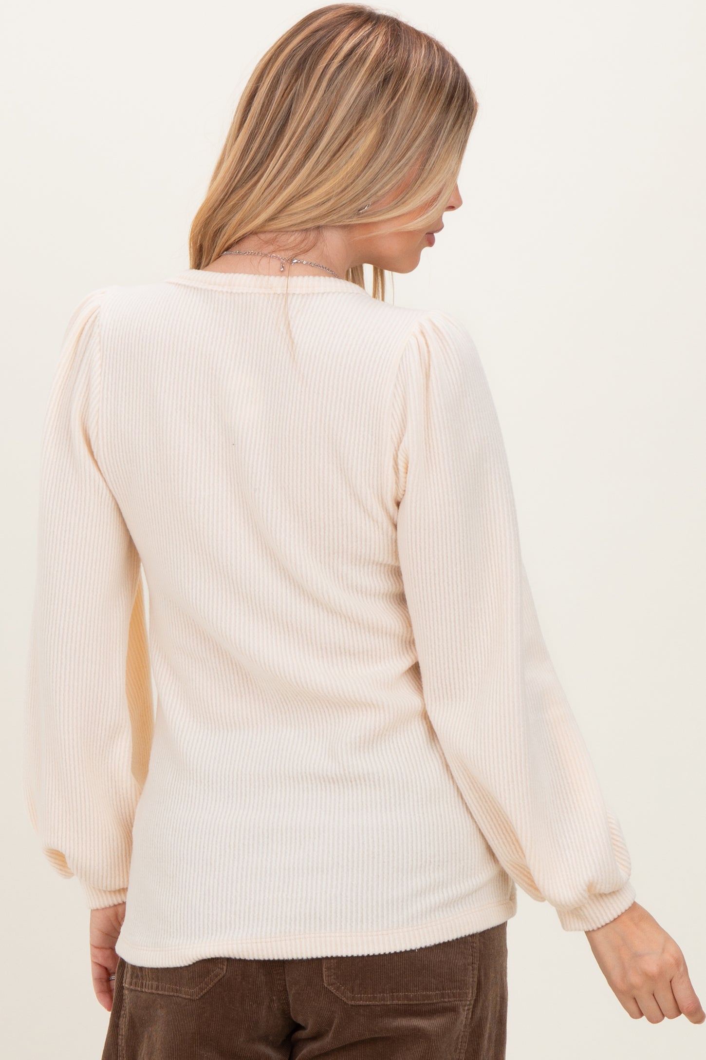 woman wearing a pale peach ribbed long sleeve top with puffed sleeves, viewed from the back
