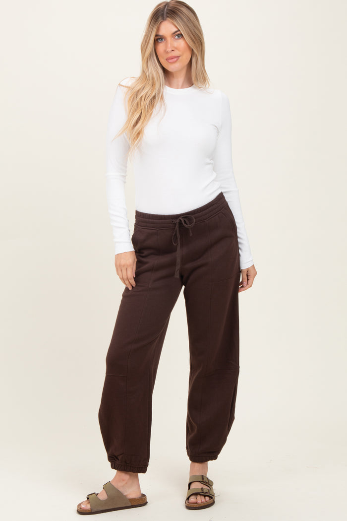 woman wearing a white long sleeve top and brown jogger pants with a drawstring, standing in a relaxed pose