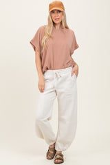 woman wearing a beige striped oversized top and cream jogger pants, styled with a brown cap and sandals