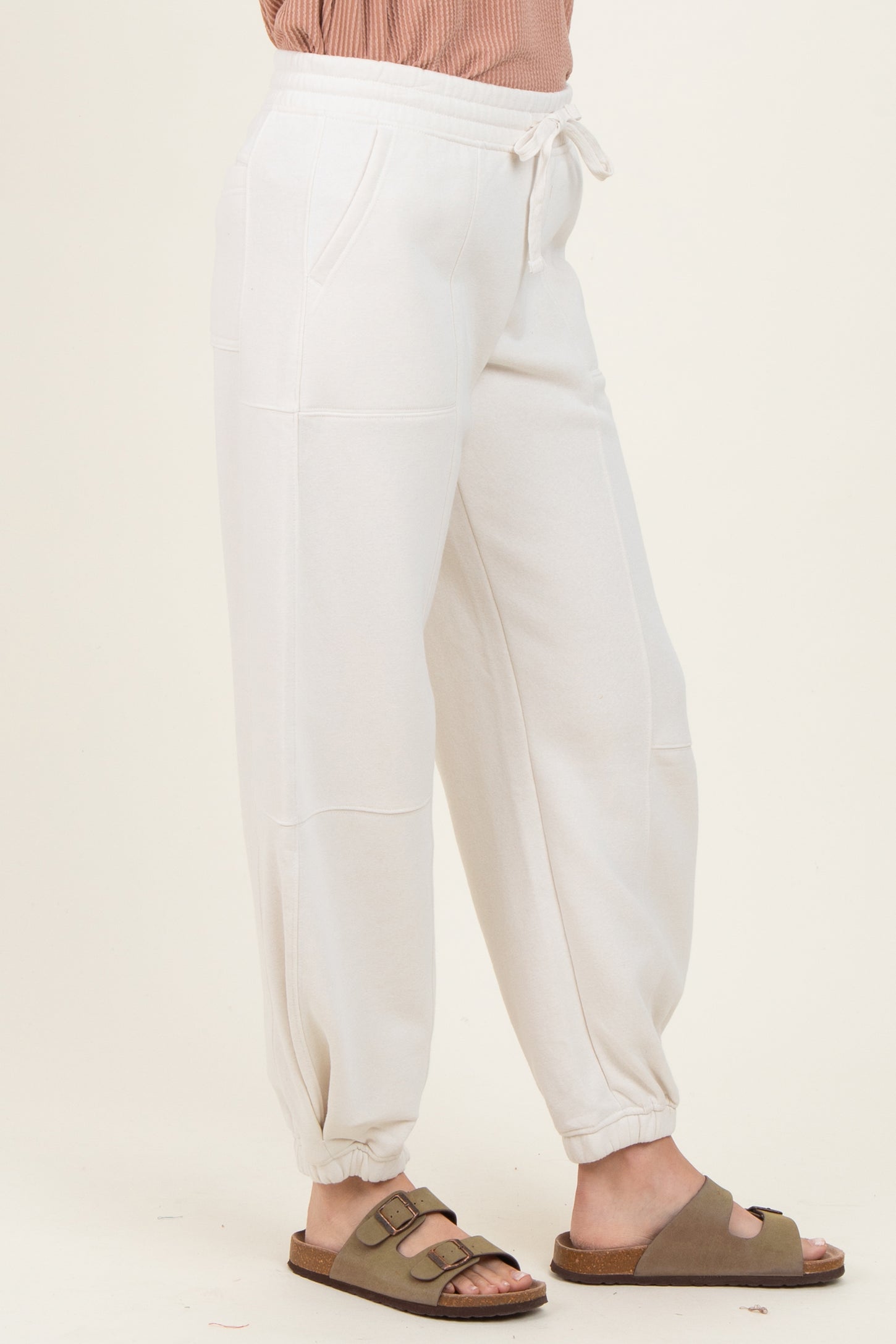 woman wearing white jogger pants with side pockets and cuffed ankles, paired with a pink top and sandals