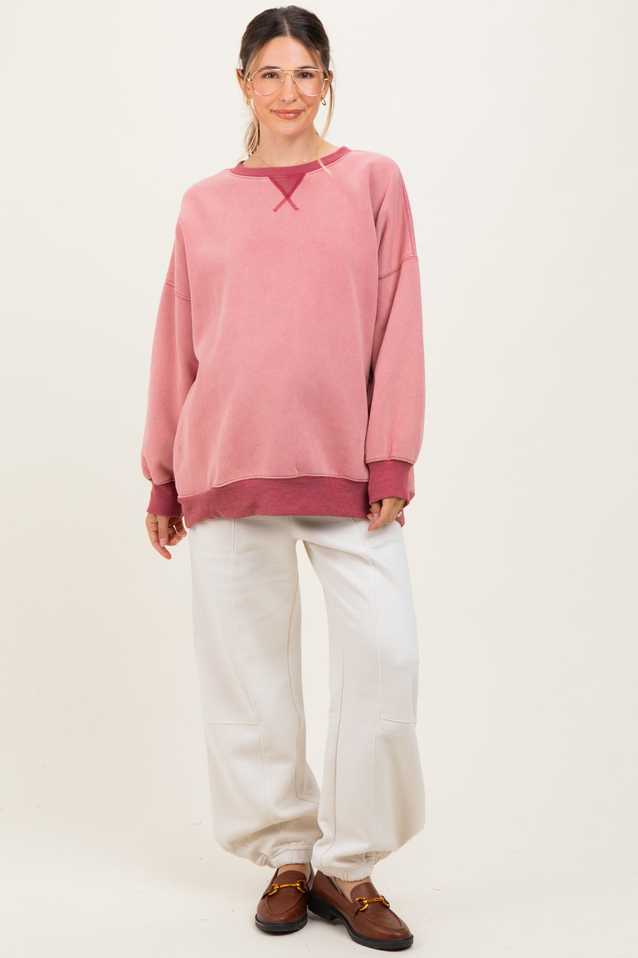 woman wearing a pink oversized maternity sweatshirt with white pants and a visible baby bump
