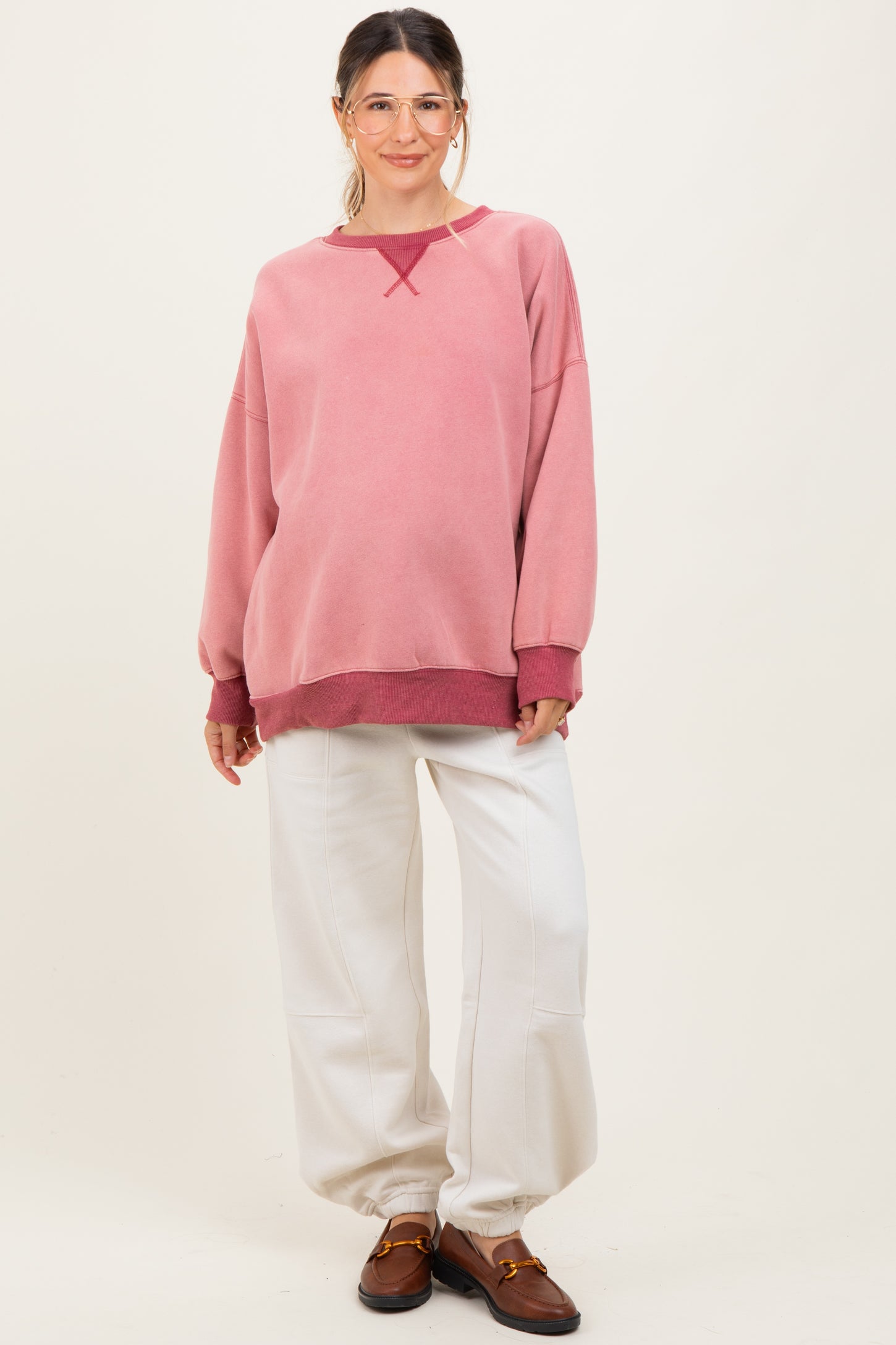 woman wearing a pink oversized maternity sweatshirt with white pants and a visible baby bump