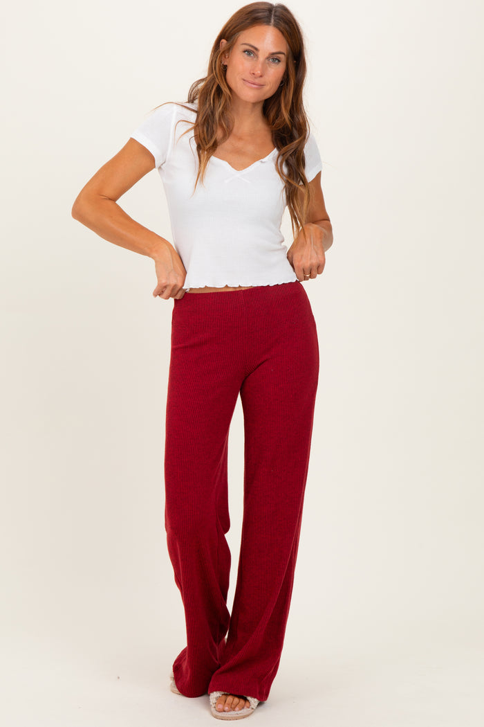 woman wearing a white short sleeve v-neck top and burgundy wide-leg pants, standing with hands on waistband