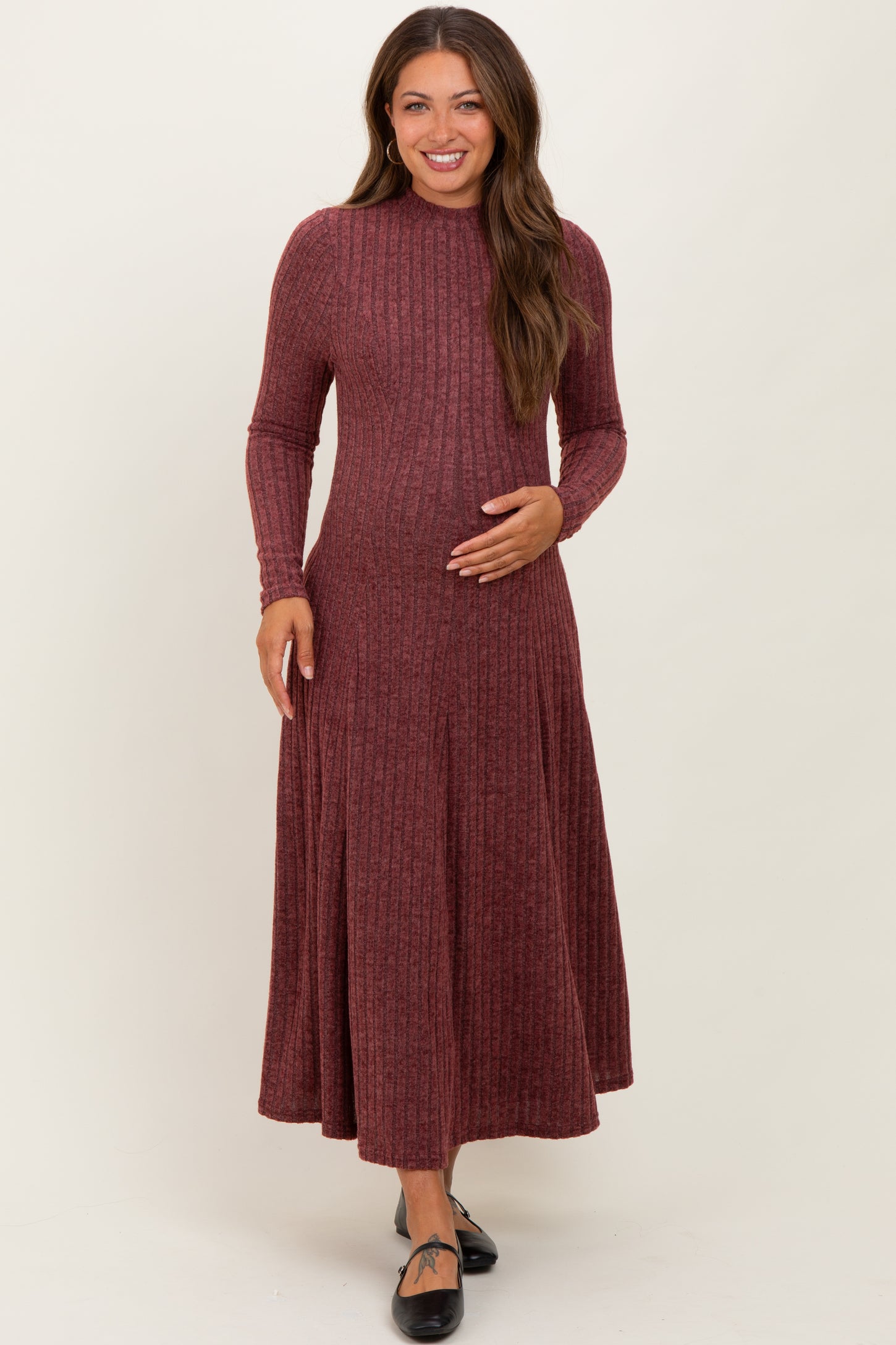 woman wearing a maroon ribbed long sleeve maternity dress and gently holding her baby bump