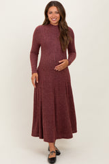 woman wearing a maroon ribbed long sleeve maternity dress and gently holding her baby bump