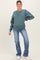 woman wearing a teal oversized maternity sweatshirt with long sleeves and distressed light blue jeans, showing her baby bump