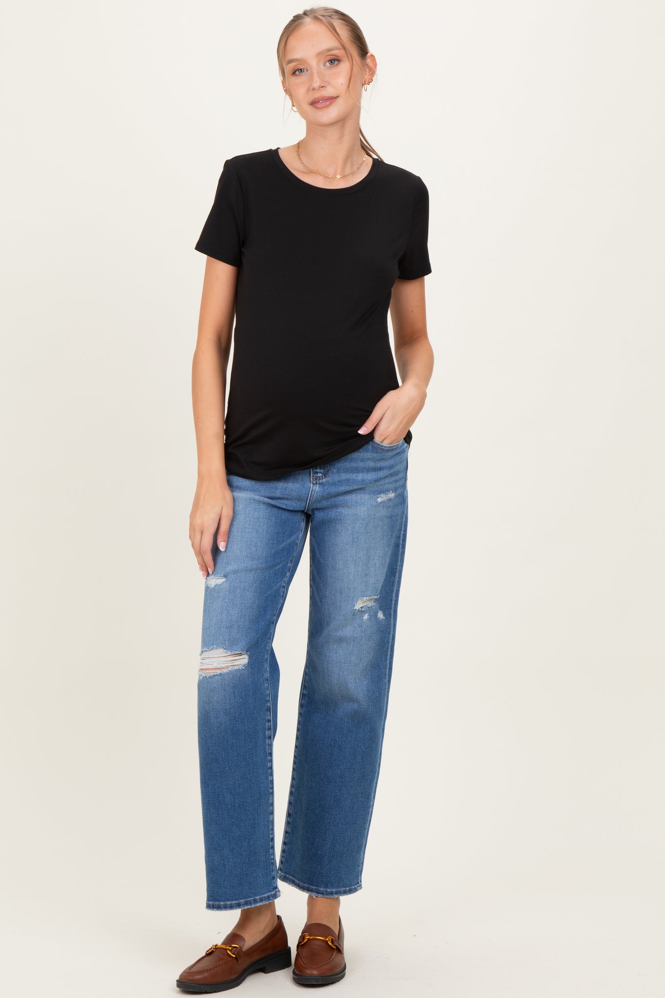 woman wearing a black short sleeve maternity top and distressed denim jeans, with a visible baby bump