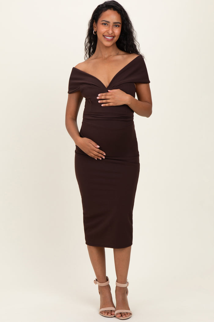 woman wearing a brown off-the-shoulder maternity dress and holding her baby bump