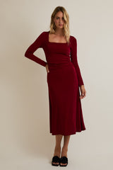 woman wearing a burgundy long sleeve midi dress with a square neckline and a side split