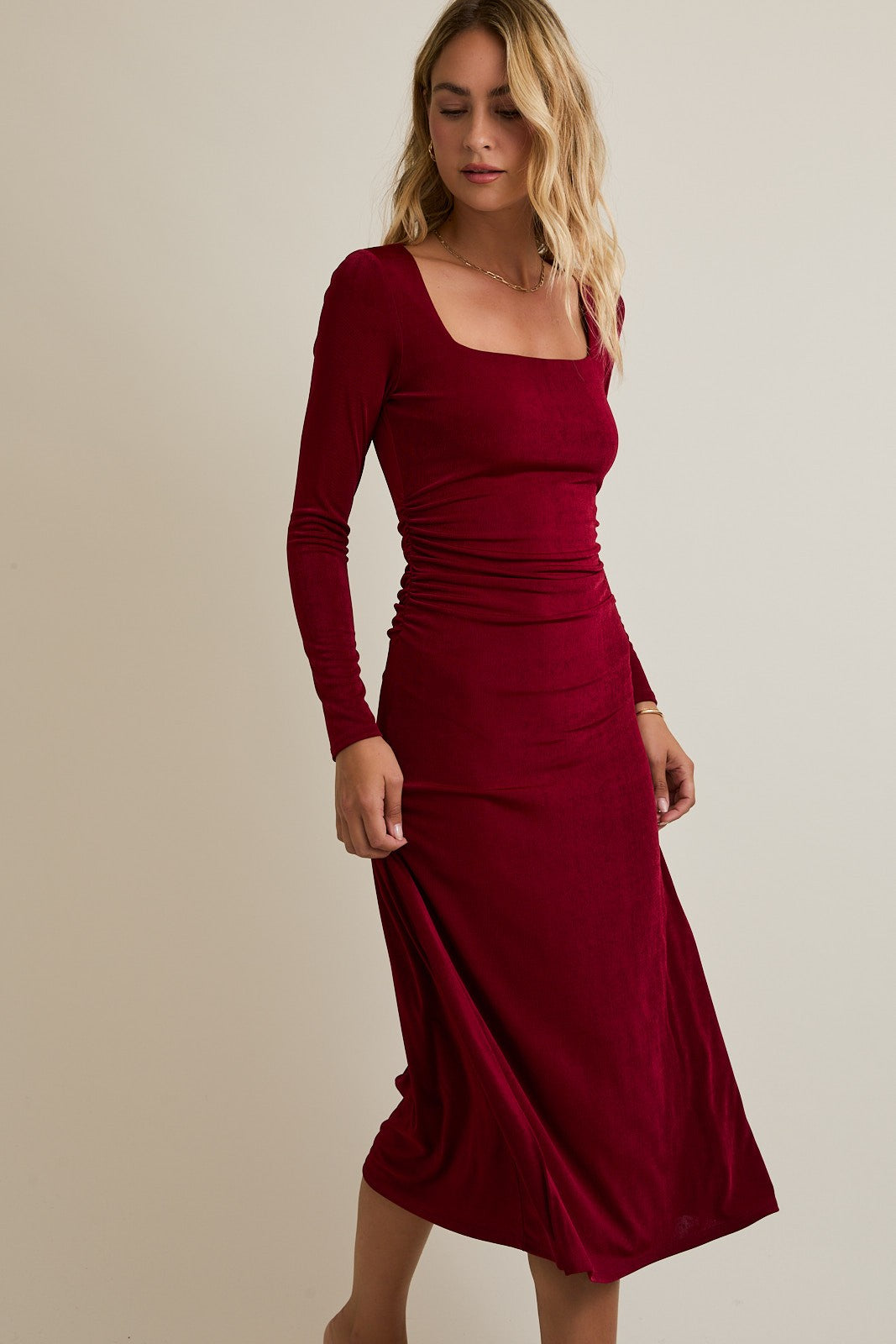 woman wearing a burgundy long sleeve midi dress with a square neckline and ruching detail