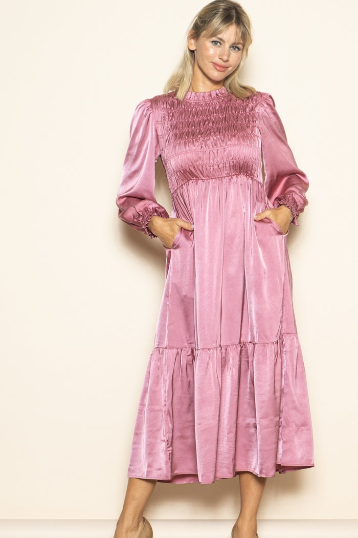 woman wearing a pink satin smocked long sleeve dress with pockets and a tiered skirt