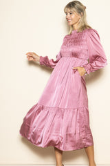 woman wearing a blush pink long sleeve smocked midi dress with a tiered hem and pockets