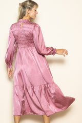woman wearing a pink satin long sleeve dress with a smocked bodice and tiered skirt, shown from the back