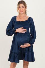 woman wearing a navy blue maternity dress with puff sleeves and a ruffled hem, holding her baby bump