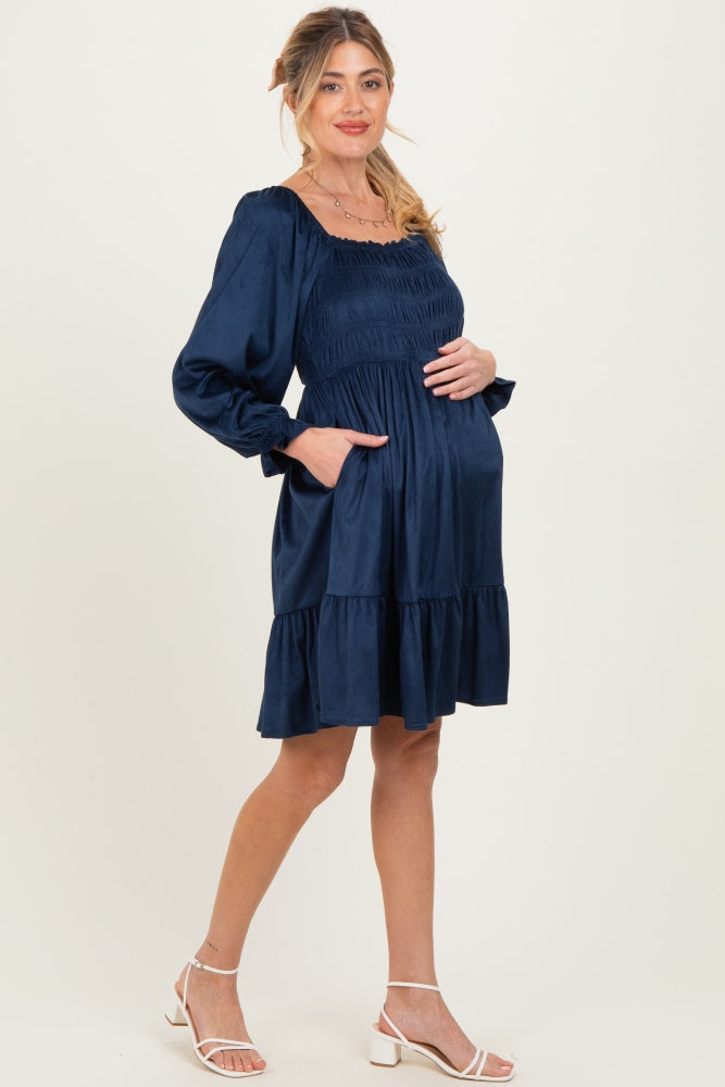 woman wearing a navy blue maternity dress with smocked bodice and tiered skirt, holding her baby bump