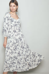 woman wearing a floral print maxi dress with puff sleeves and a tiered hem, smiling and posing gracefully