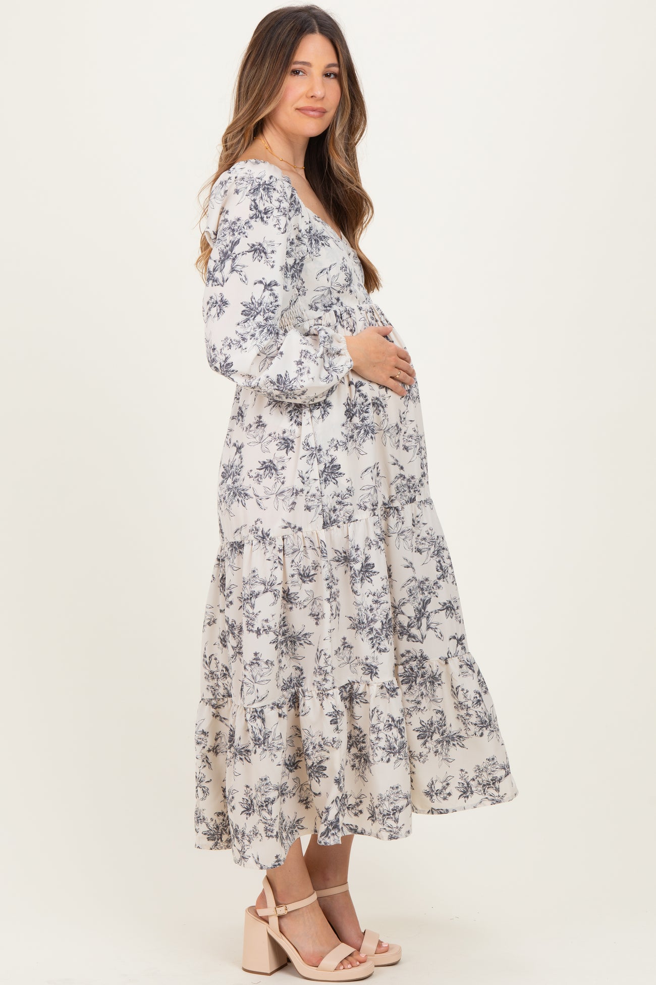 woman wearing a floral print long sleeve maternity dress with a tiered skirt and holding her baby bump