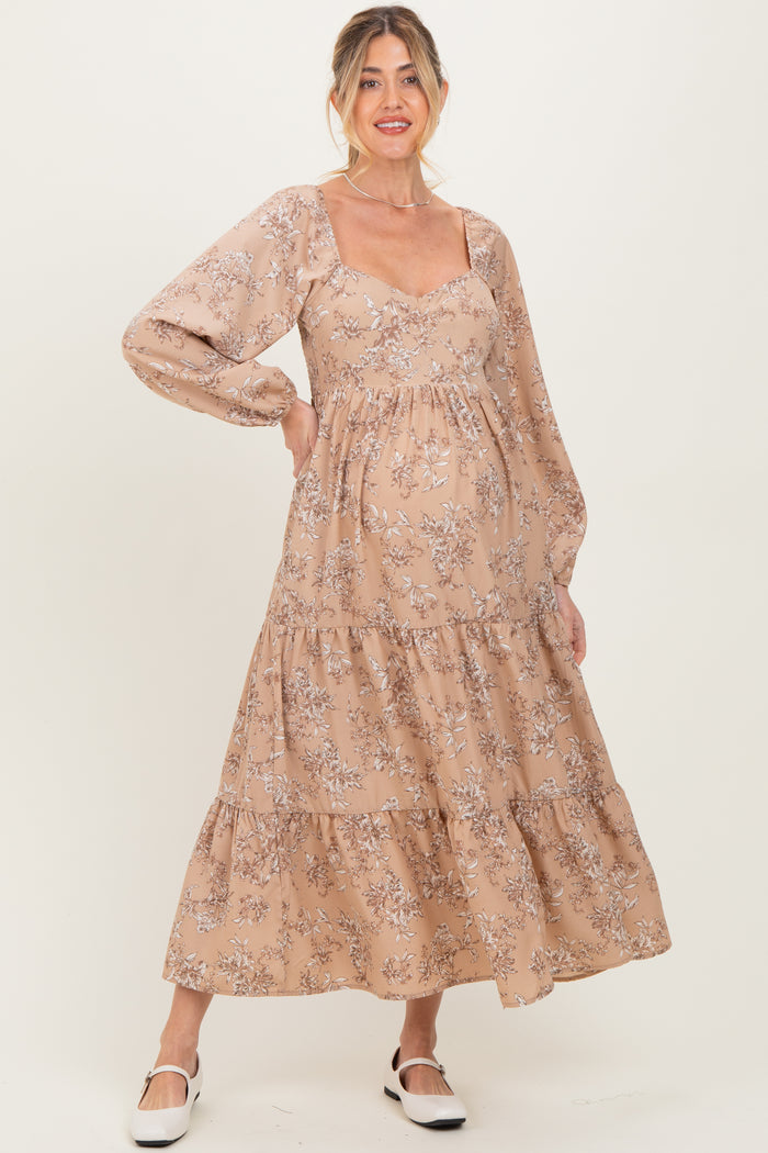 woman wearing a light brown floral maternity dress with long sleeves and a tiered skirt, highlighting her baby bump