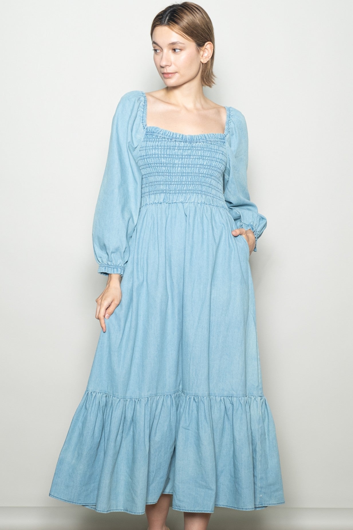 woman wearing a light blue smocked denim dress with long sleeves and a tiered skirt