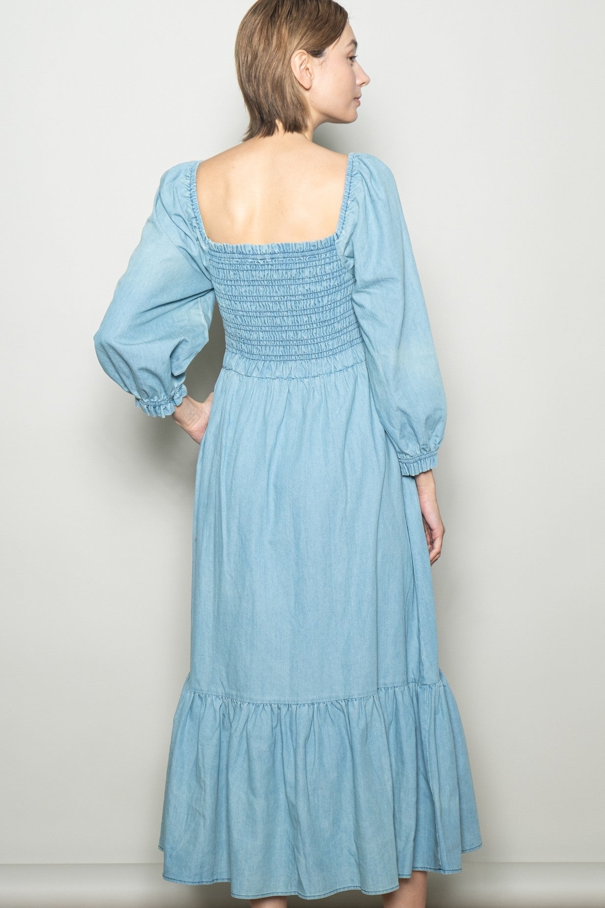 woman wearing a light blue denim maxi dress with a smocked bodice and puff sleeves, view from the back