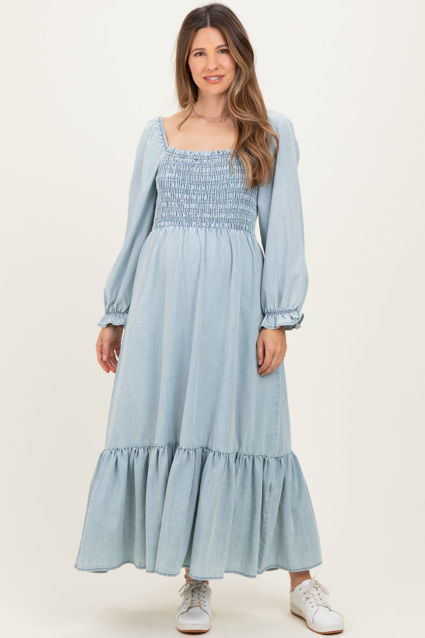 woman wearing a light blue maternity maxi dress with a smocked bodice and puff sleeves, standing against a neutral background