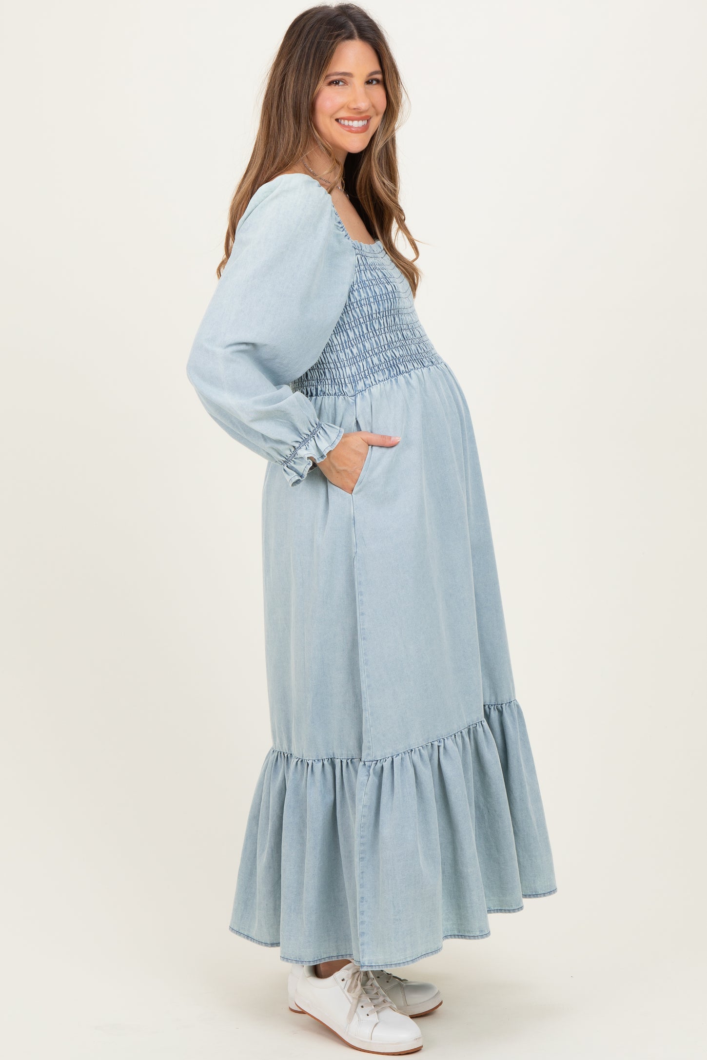 woman wearing a light blue denim maternity maxi dress with smocked bodice and puff sleeves, showing her baby bump