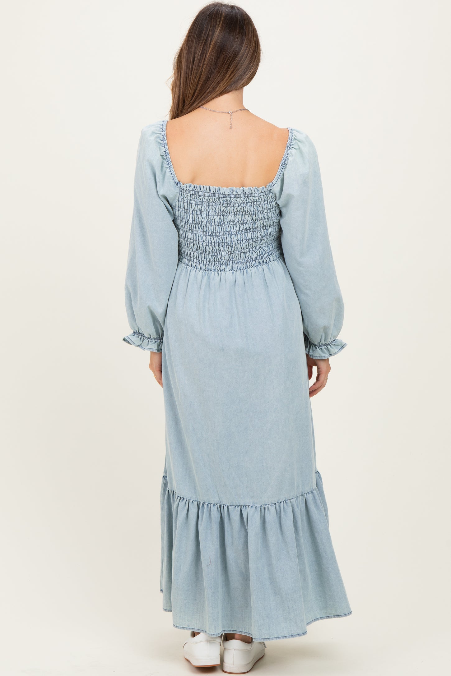 woman wearing a light blue maternity maxi dress with a smocked bodice and long sleeves, back view