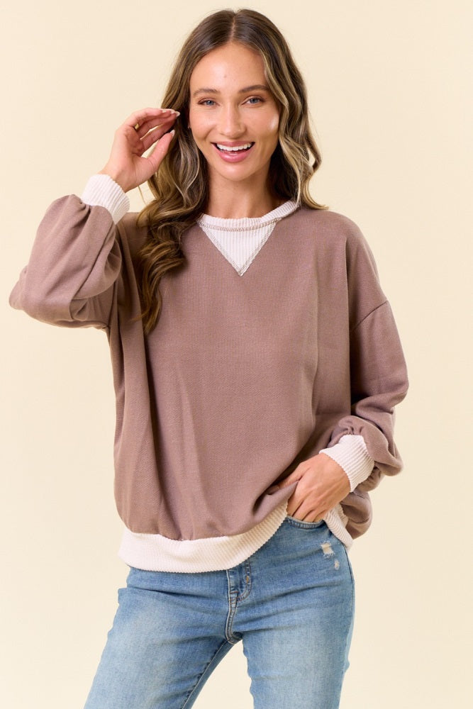 woman wearing a taupe oversized sweatshirt with white banded cuffs and hem, styled with light blue jeans