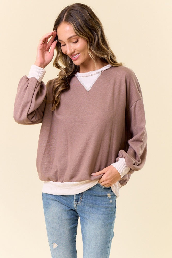 woman wearing a brown oversized pullover sweater with puff sleeves and white trim, paired with light blue jeans