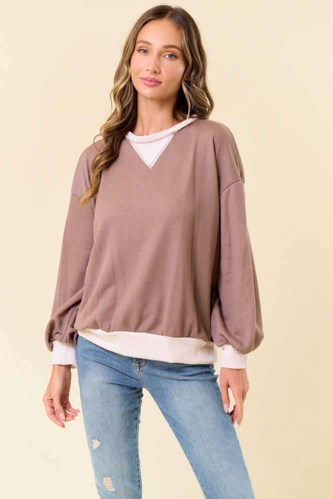 woman wearing a taupe oversized sweatshirt with balloon sleeves and a white trim, paired with light blue jeans
