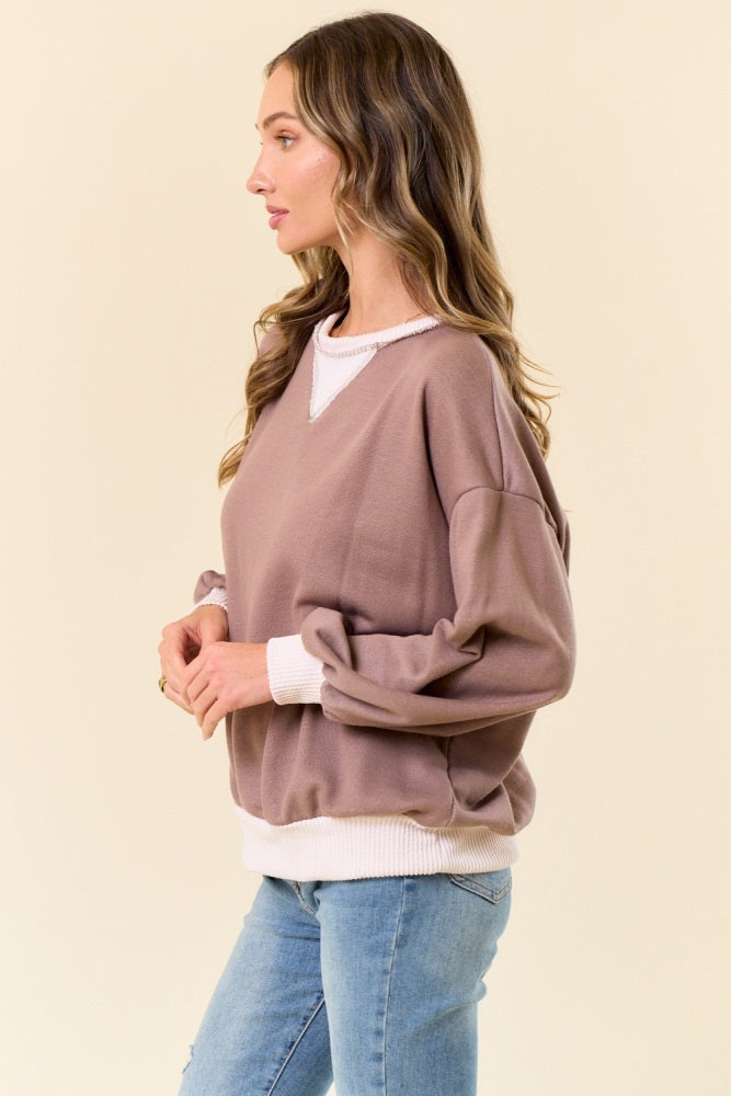 woman wearing a taupe oversized sweatshirt with a white neckline and cuffs, paired with light blue jeans