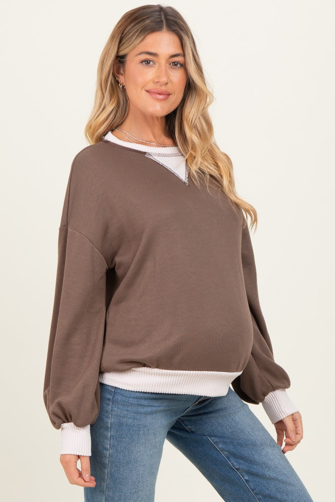 woman wearing a brown maternity sweatshirt with puff sleeves and white ribbed cuffs, displaying her baby bump