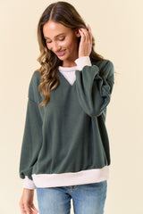 woman wearing a forest green v-neck sweater with light pink ribbed trim and balloon sleeves, smiling and touching her hair