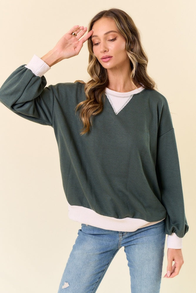 woman wearing a green oversized sweatshirt with white ribbed detailing and light blue skinny jeans